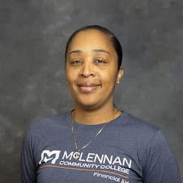 Smiling person wearing a McLennan Community College “Financial Aid” T-shirt against a gray studio backdrop.
